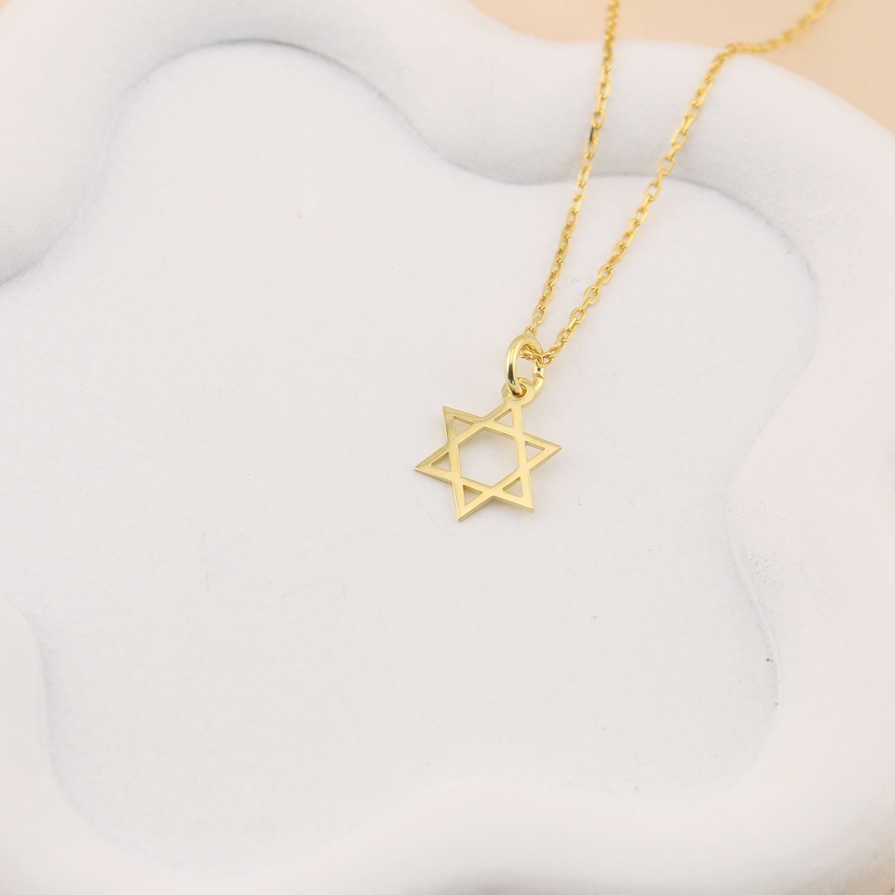 Gold necklace with a Star of David pendant on a white stone surface