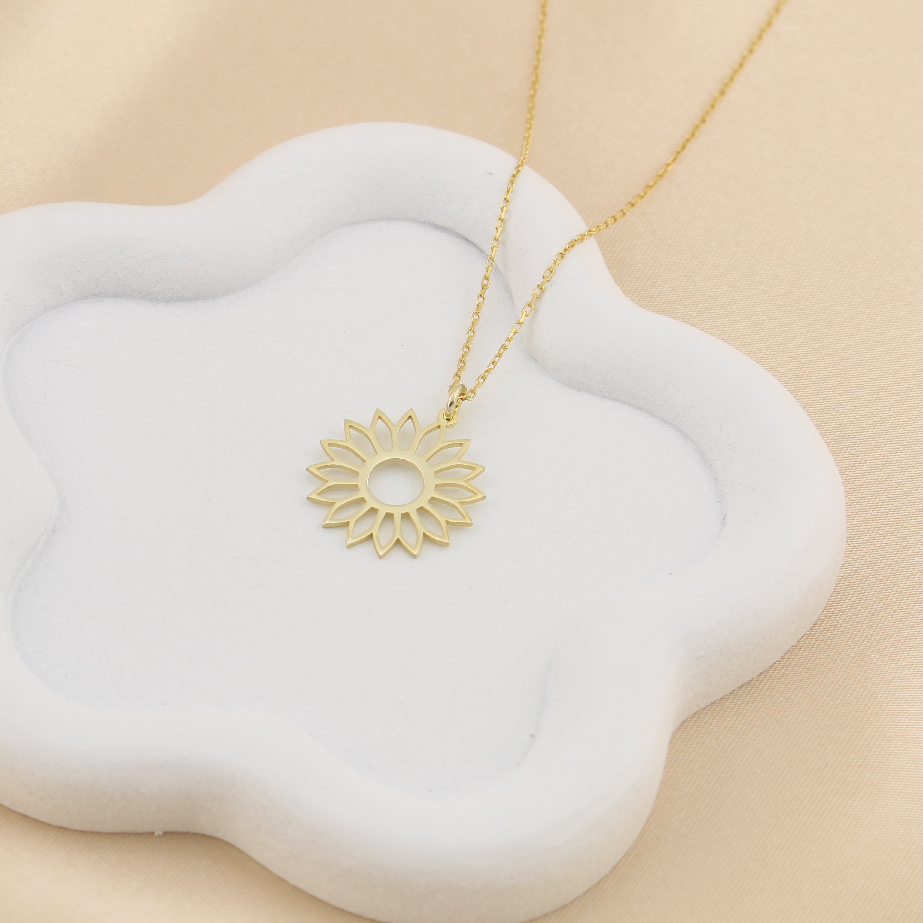 Gold necklace with a sunflower pendant on a white cloud-shaped stand against a beige background