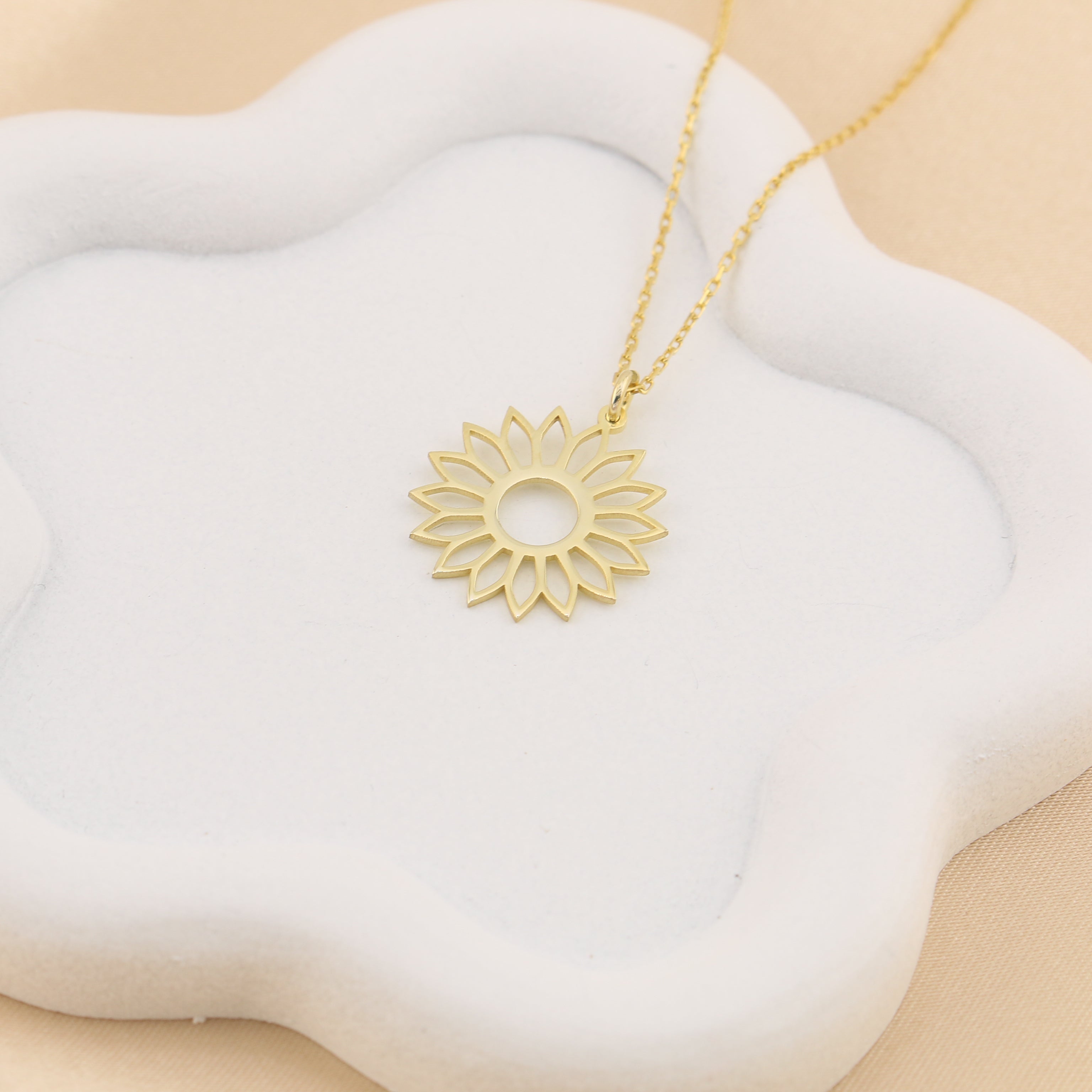 Gold necklace with a sunflower pendant on a white cloud-shaped stand against a beige background