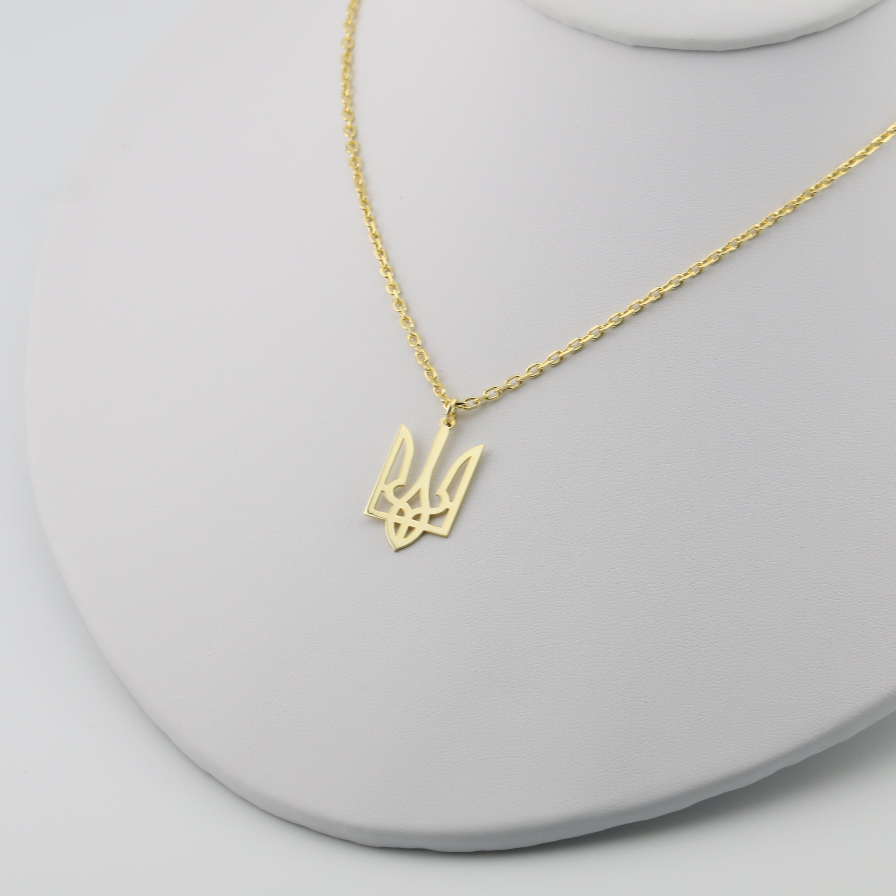 Gold trident necklace on a cable chain on a white stand