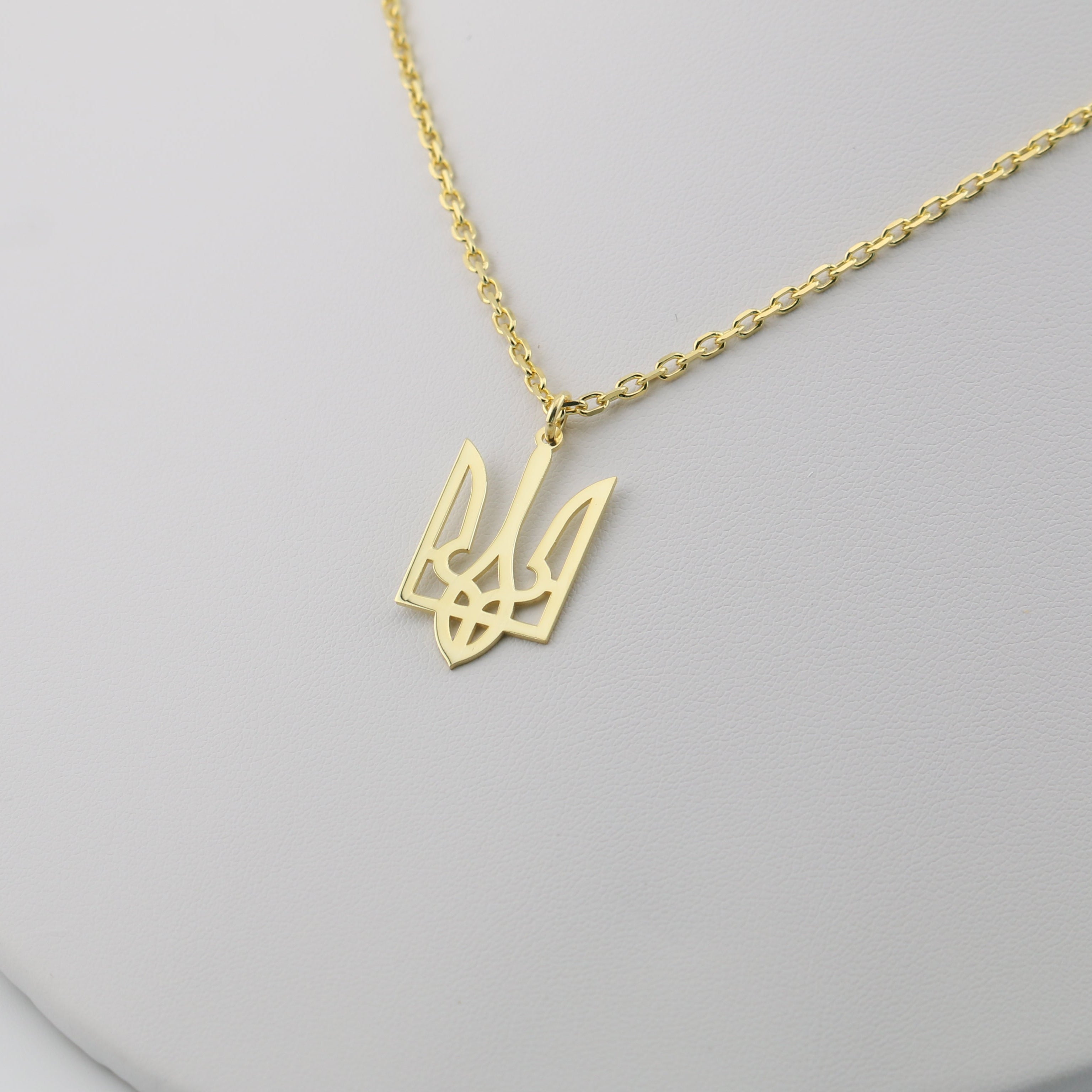 Gold necklace with a trident pendant on a light gray background