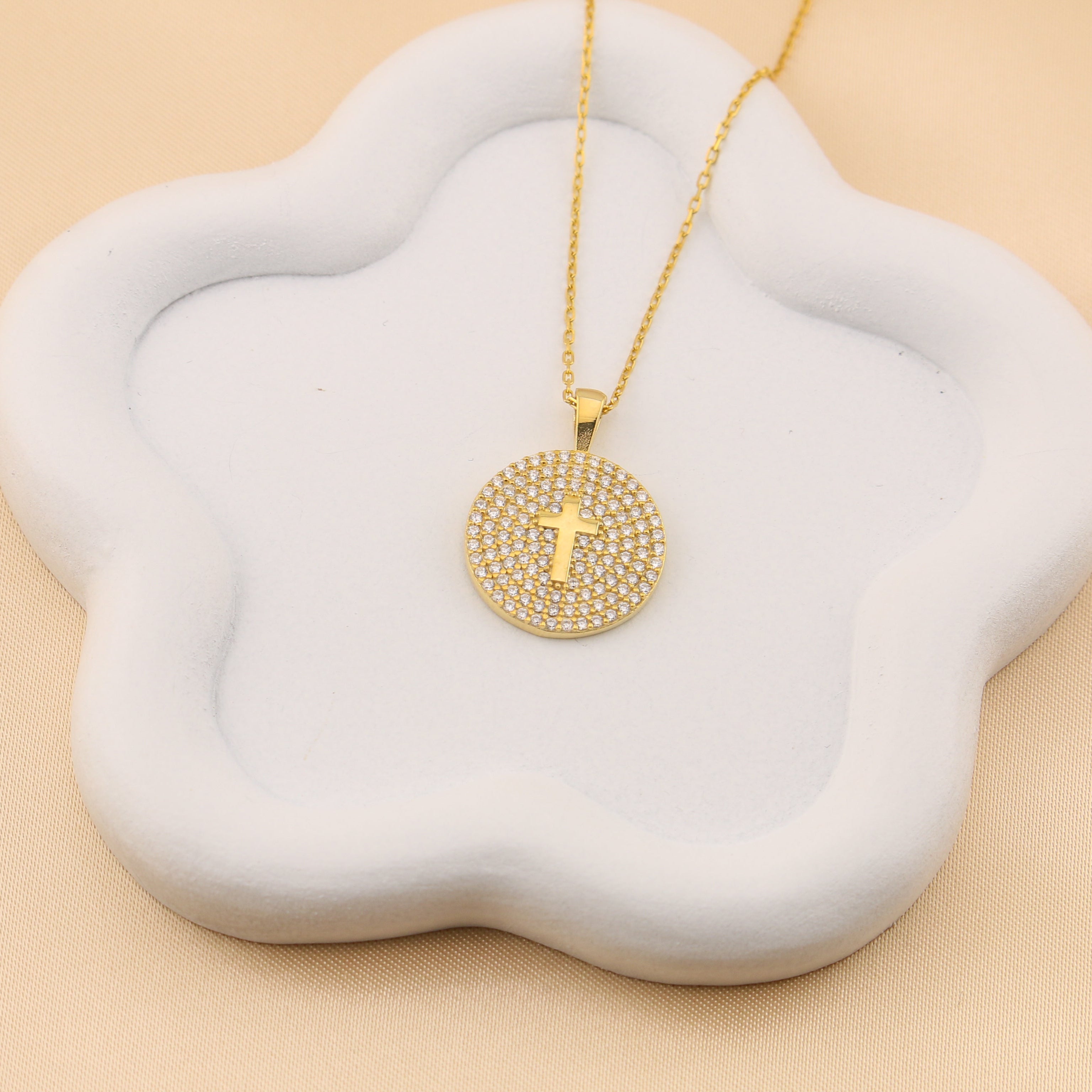 Gold necklace with a cross pendant on a white floral stand against a beige background