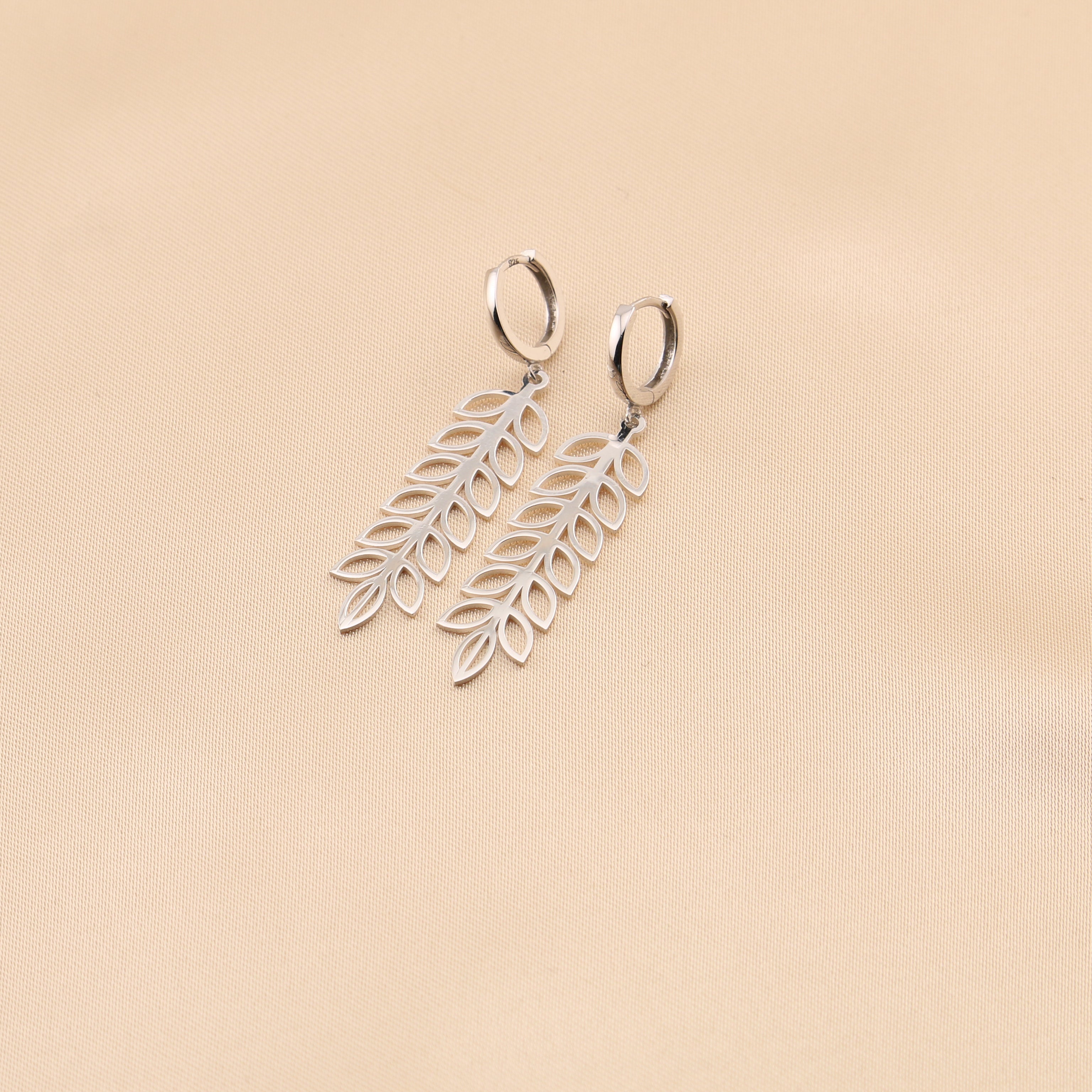 Silver leaf-shaped earrings on a beige background