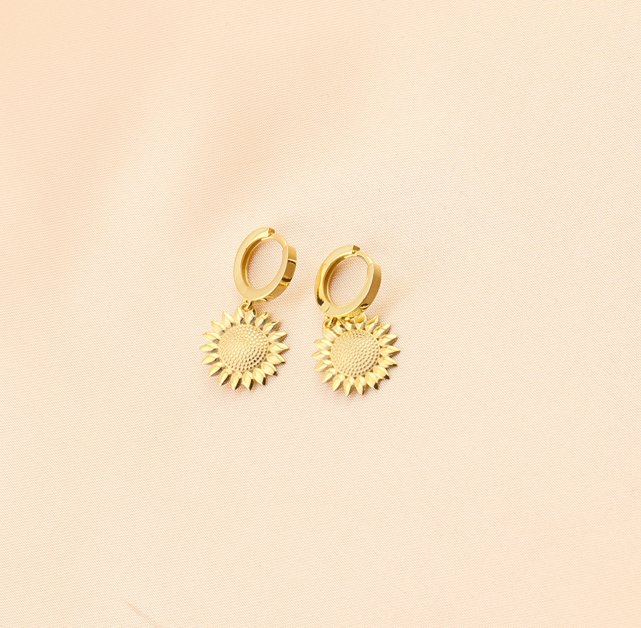 Gold sun-shaped earrings on a beige background