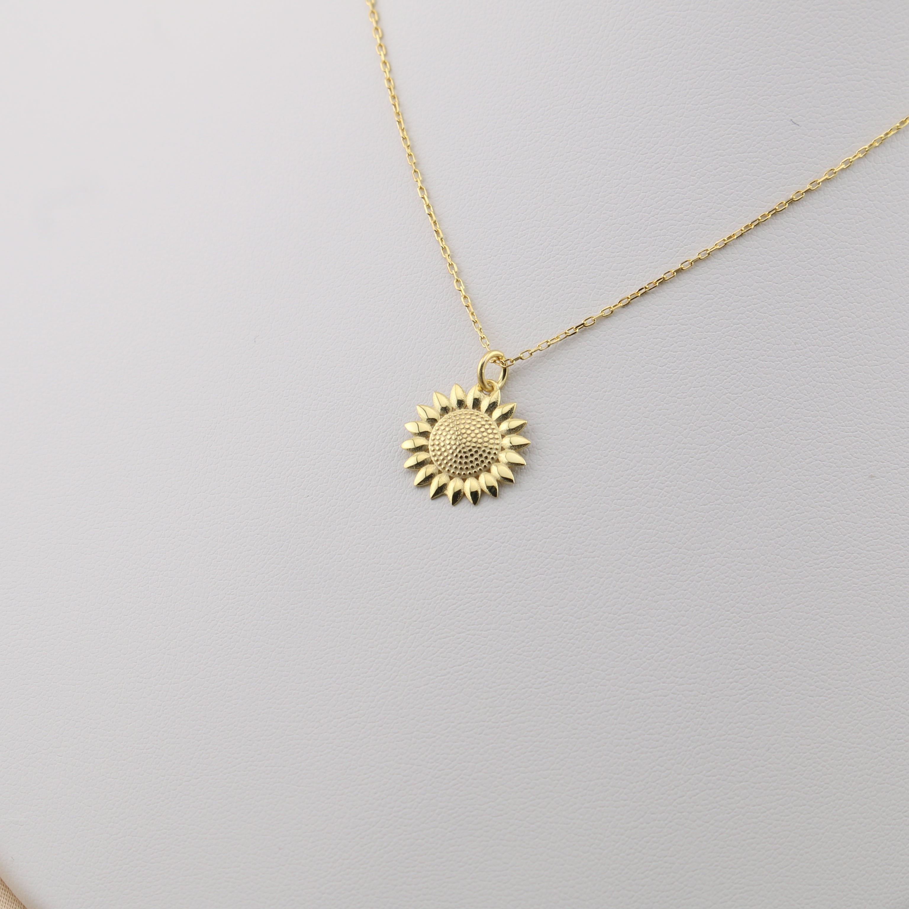 Gold sunflower pendant necklace on a white stand with a beige background