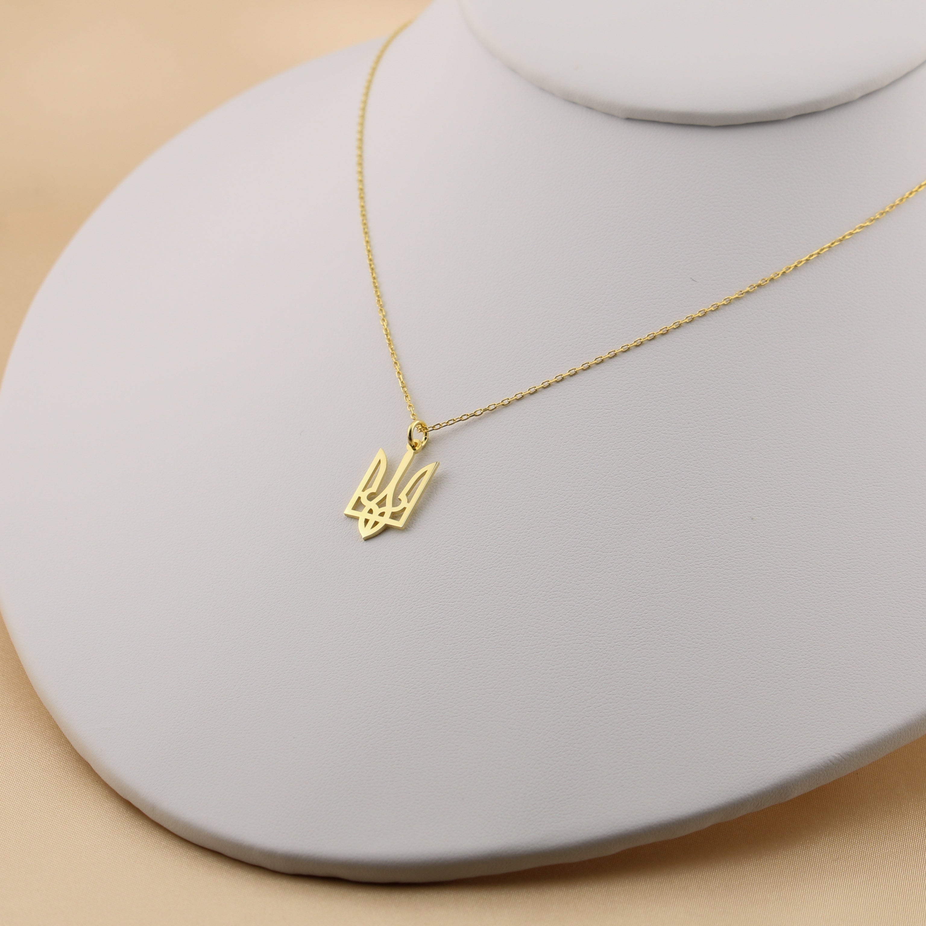 Gold necklace with a small pendant on a gray stand against a beige background