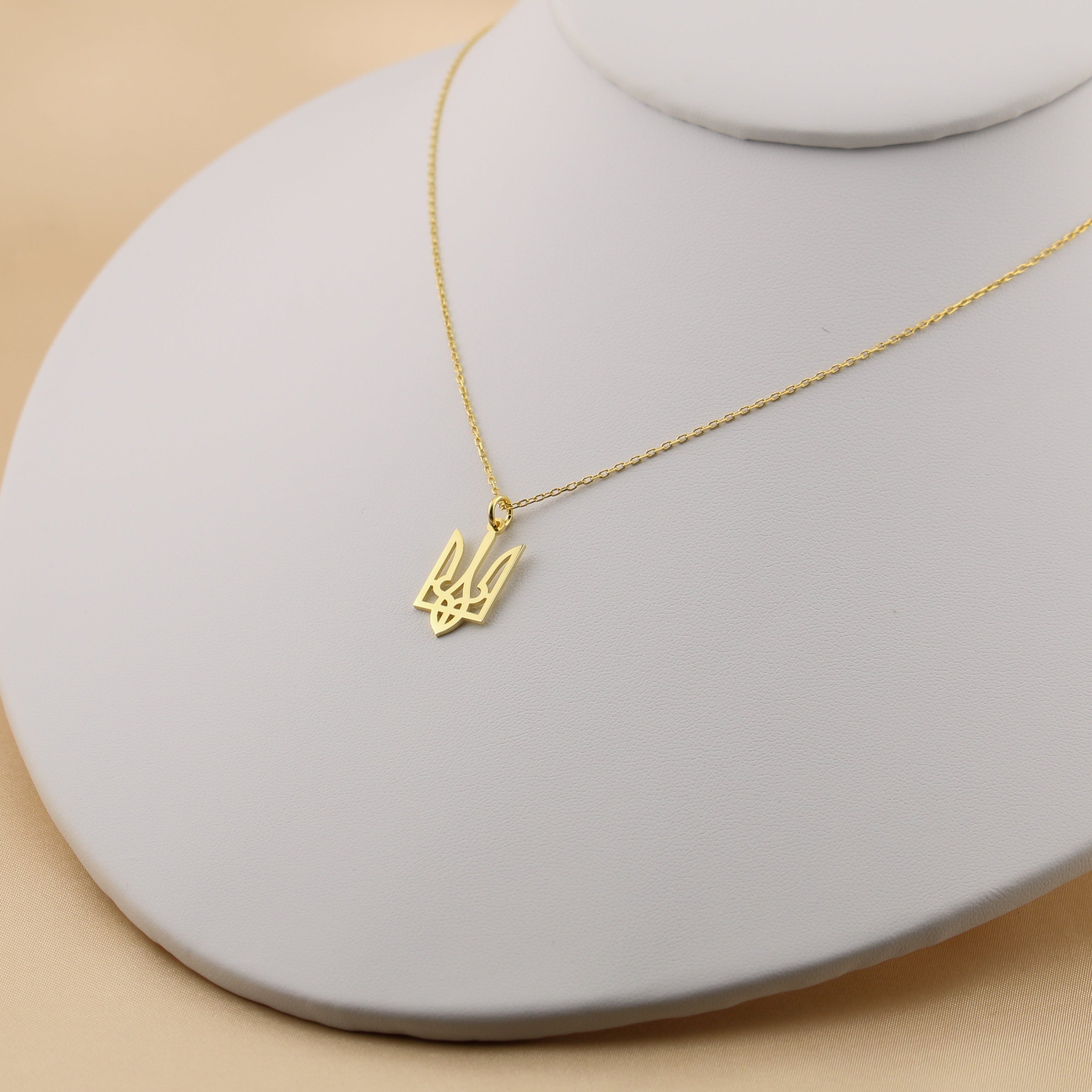 Gold necklace with a small pendant on a gray stand against a beige background
