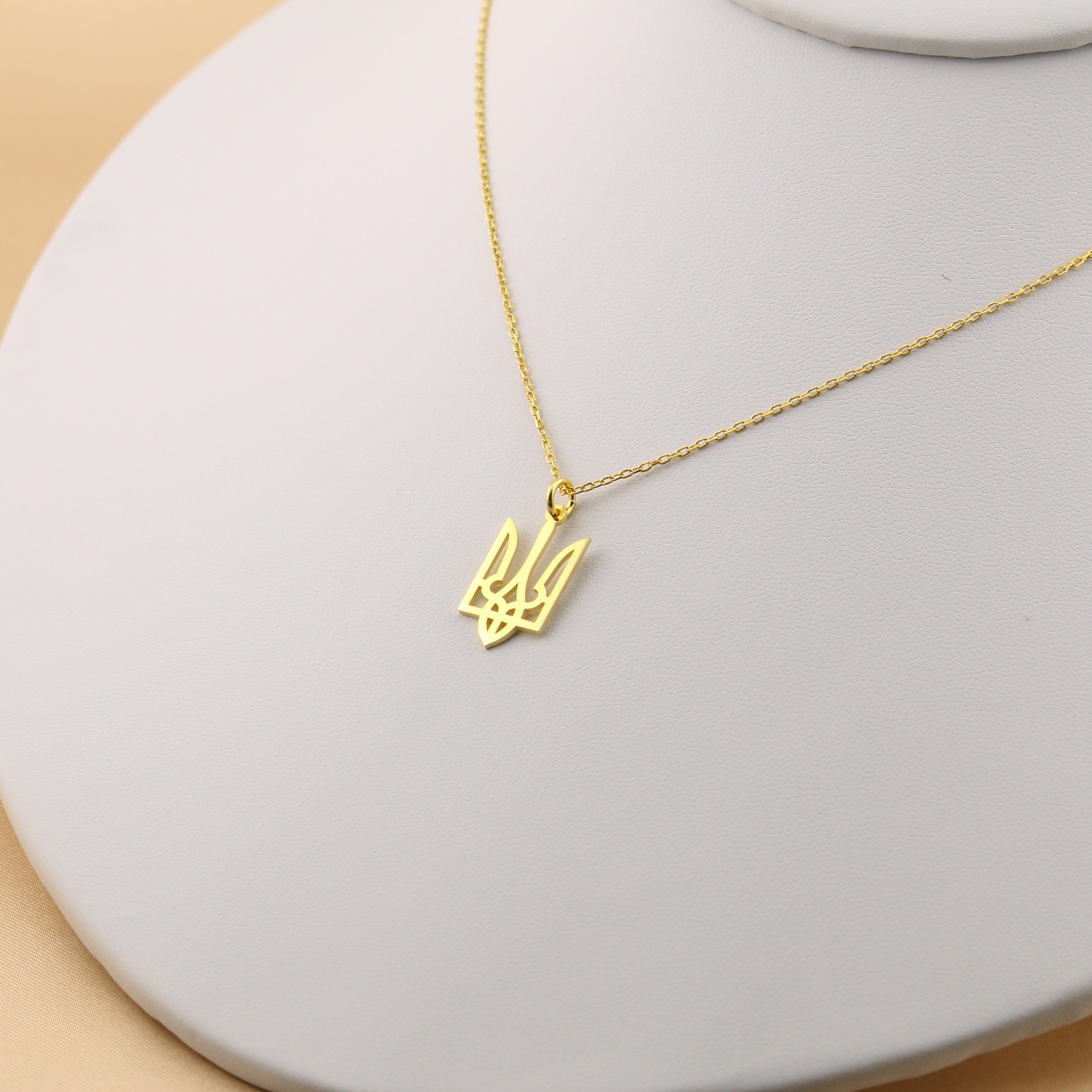 Gold necklace with a pendant on a light gray stand against a beige background