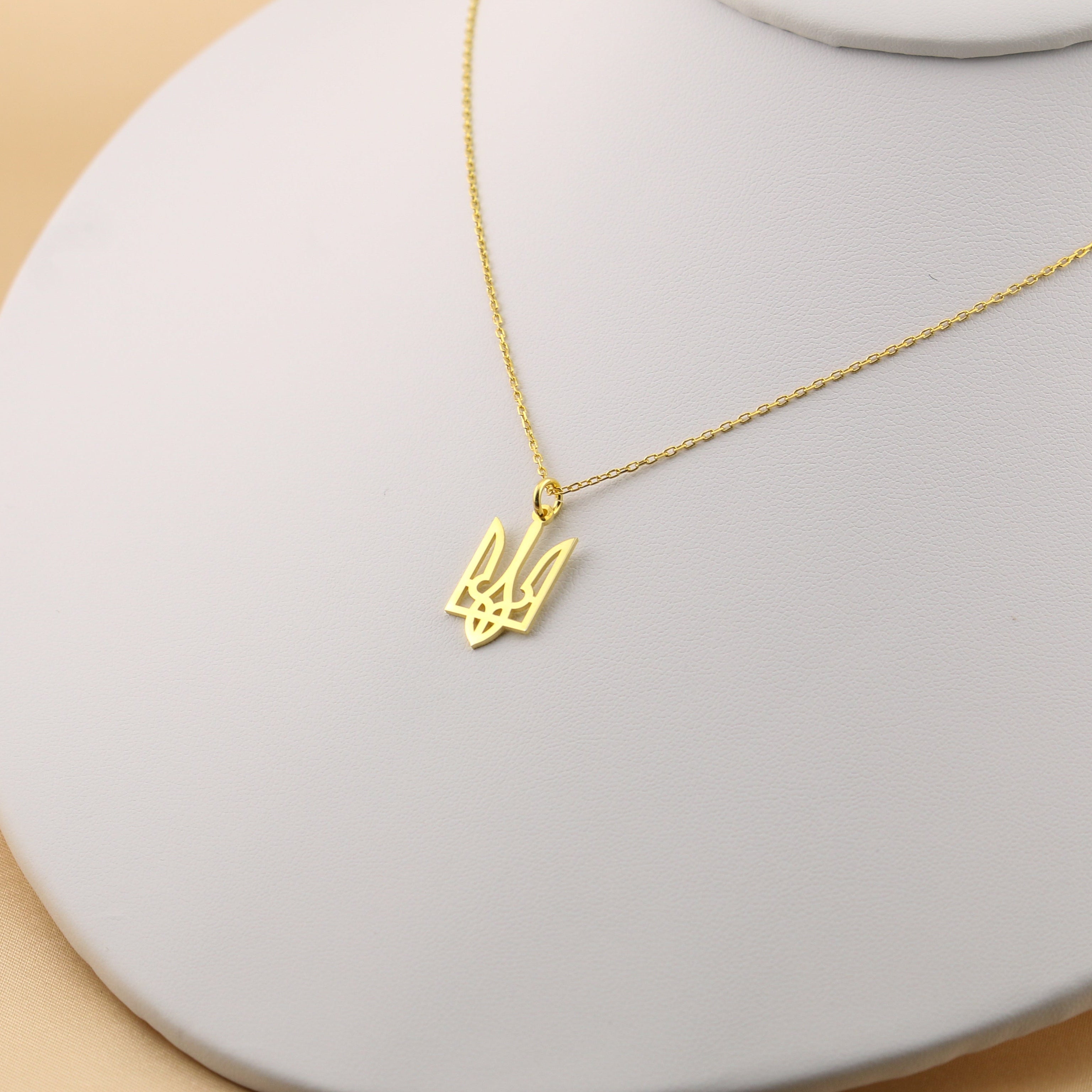 Gold necklace with a pendant on a light gray stand against a beige background