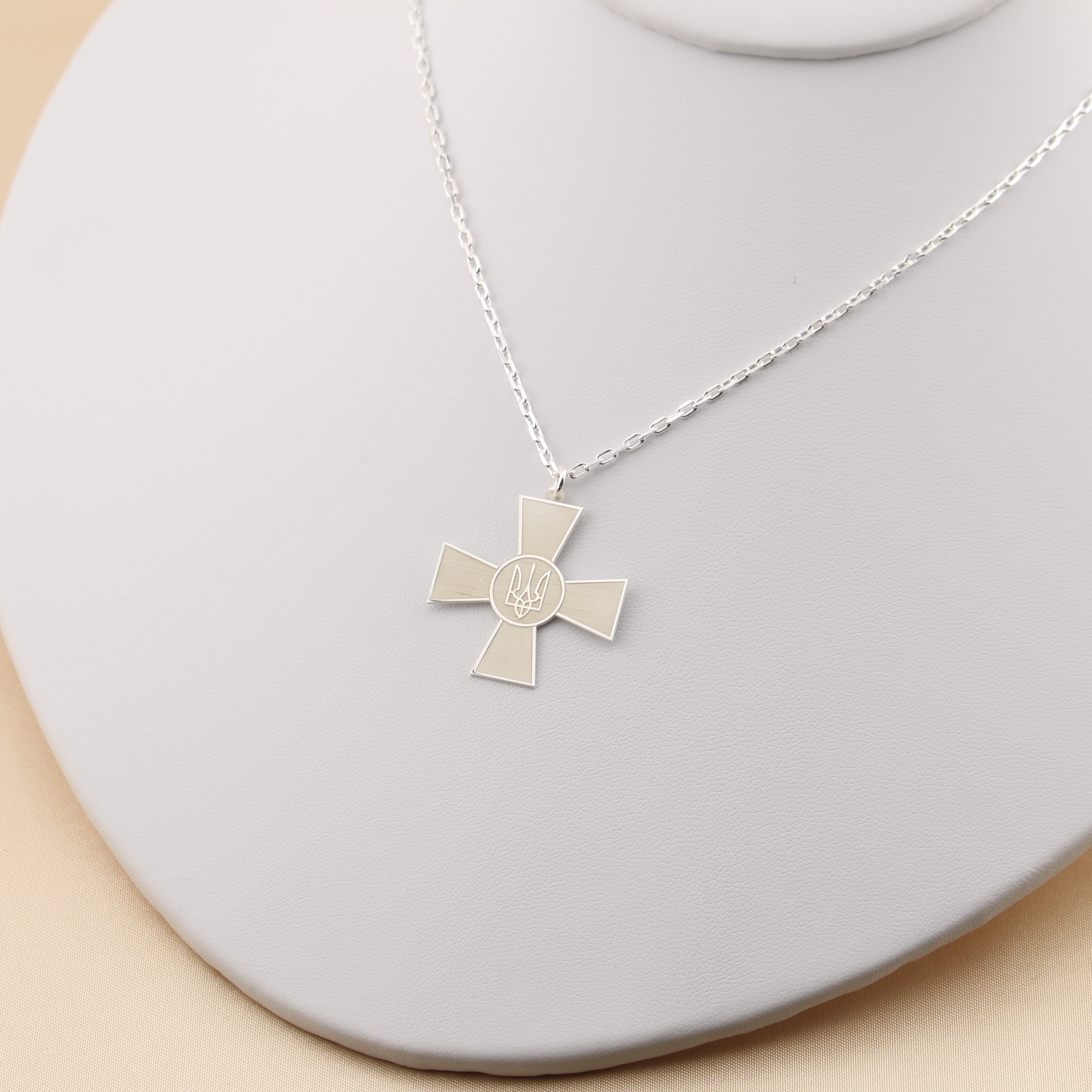 Silver cross necklace on a gray stand with a beige background