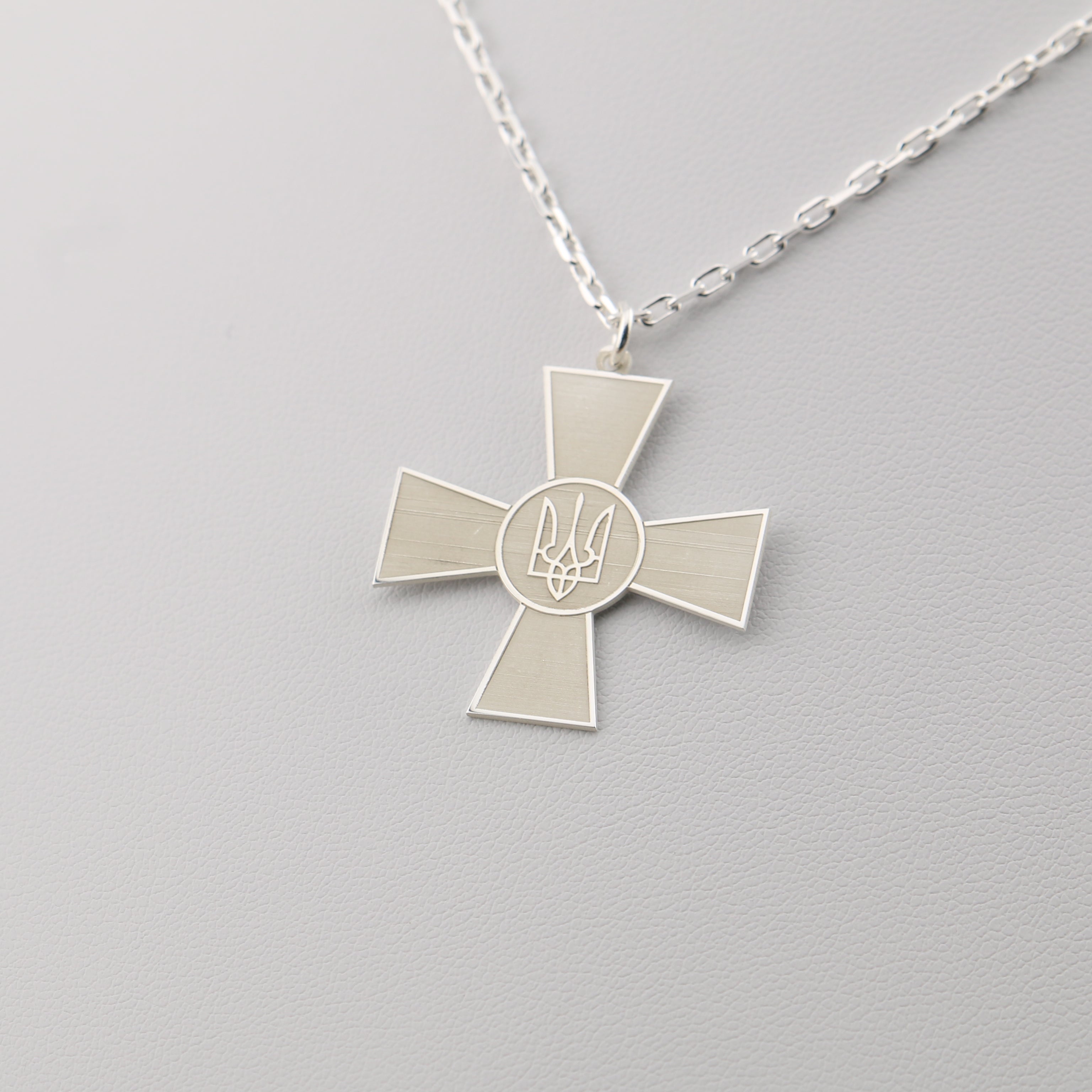 Silver cross-shaped pendant necklace on a light gray background